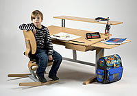 Sch&uuml;lerschreibtisch Moizi 17 mit zus&auml;tzlichen Ablagen hinten und rechts. Der Sch&uuml;ler sitzt auf dem Stuhl Moizi 6.