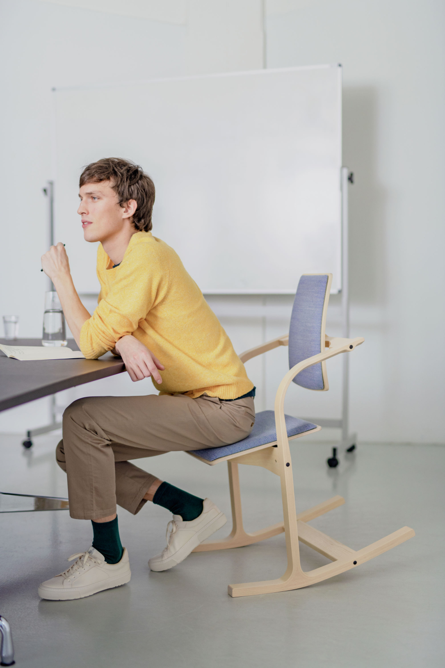 Junger Mann sitzt auf der Vorderkante eines Stokke Actulum Kufenstuhl